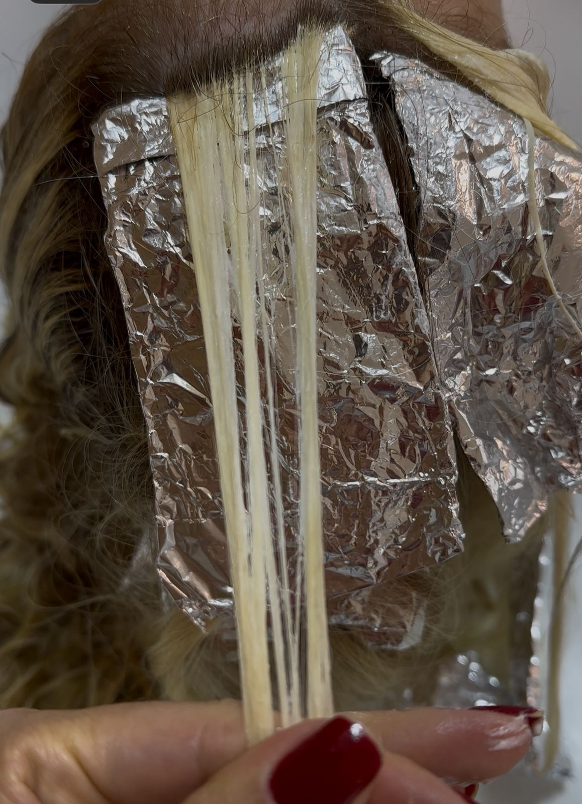 Mechas de cabelo separadas em papel alumínio durante processo de coloração, mostrando a aplicação técnica da fórmula fio a fio